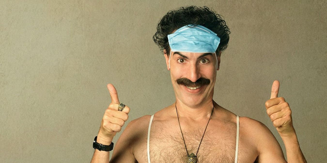 Cropped poster for Borat 2 where Sacha Baron Cohen has 2 thumbs up and wears face mask on forehead