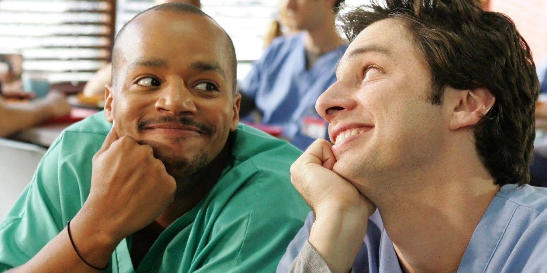 Christopher Turk and JD in Scrubs sitting side by side and smiling at each other.