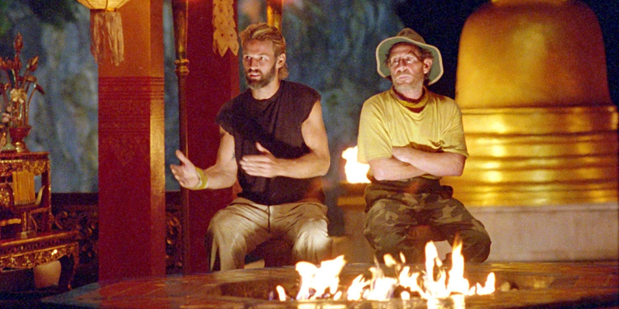 Two men sit in front of a fire