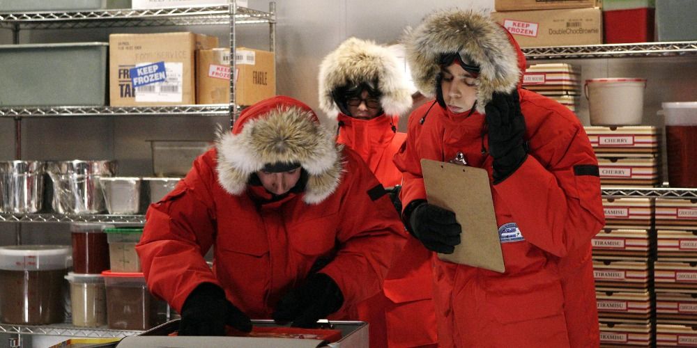 Leonard, Howard, and Sheldon in The Big Bang Theory. They are shown wearing orange hooded coats and standing in the freezer