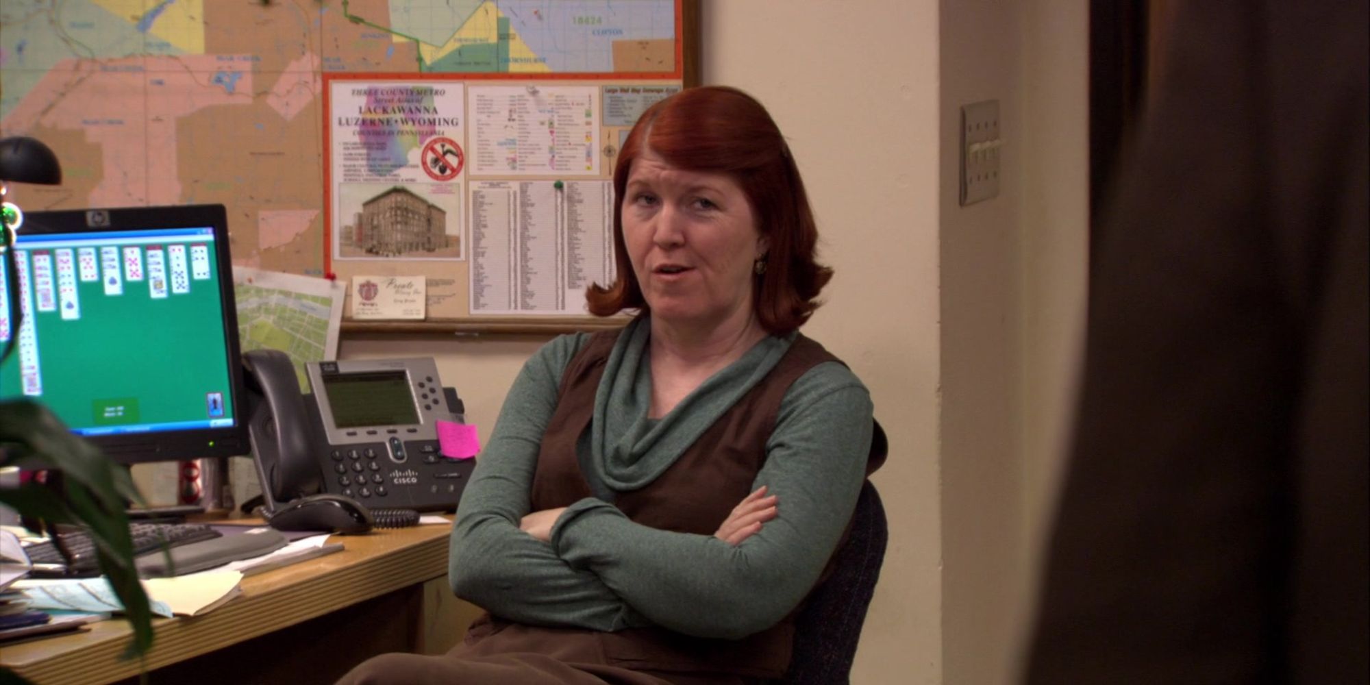 Meredith Palmer with her arms folded at her desk in The Office
