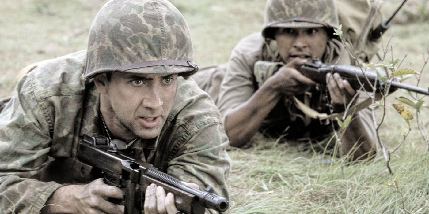 Nicolas Cage's character and another soldier holding guns, lying on the grass in Windtalkers