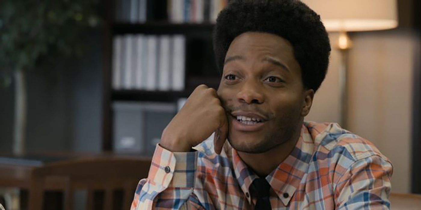 Lavelle with an afro sitting at a desk with his hand on his cheek during his job interview back in New York