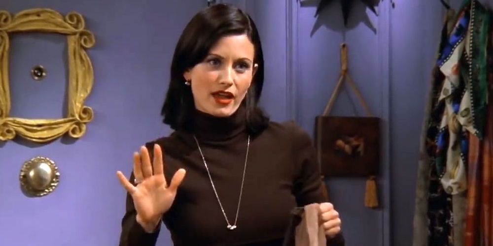 Courtney Cox with hand up and talking by door of apartment in Friends