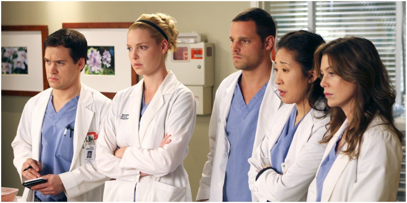 George, Izzie, Alex, Cristina, and Meredith in Grey's Anatomy. They are all dressed in their light blue scrubs and are wearing a white lab coat