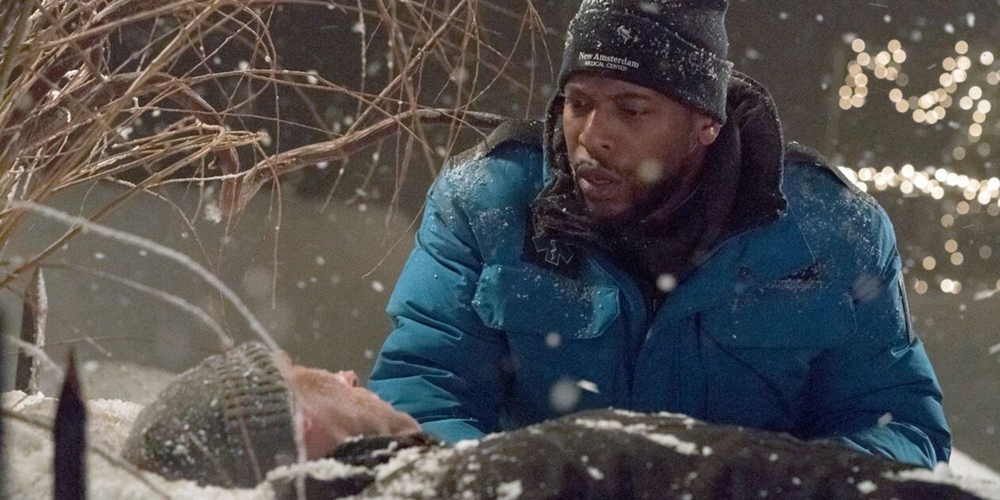 Dr. Reynolds outside in a blizzard, wearing a puffy blue jacket and winter hat helping a patient who is lying on the ground