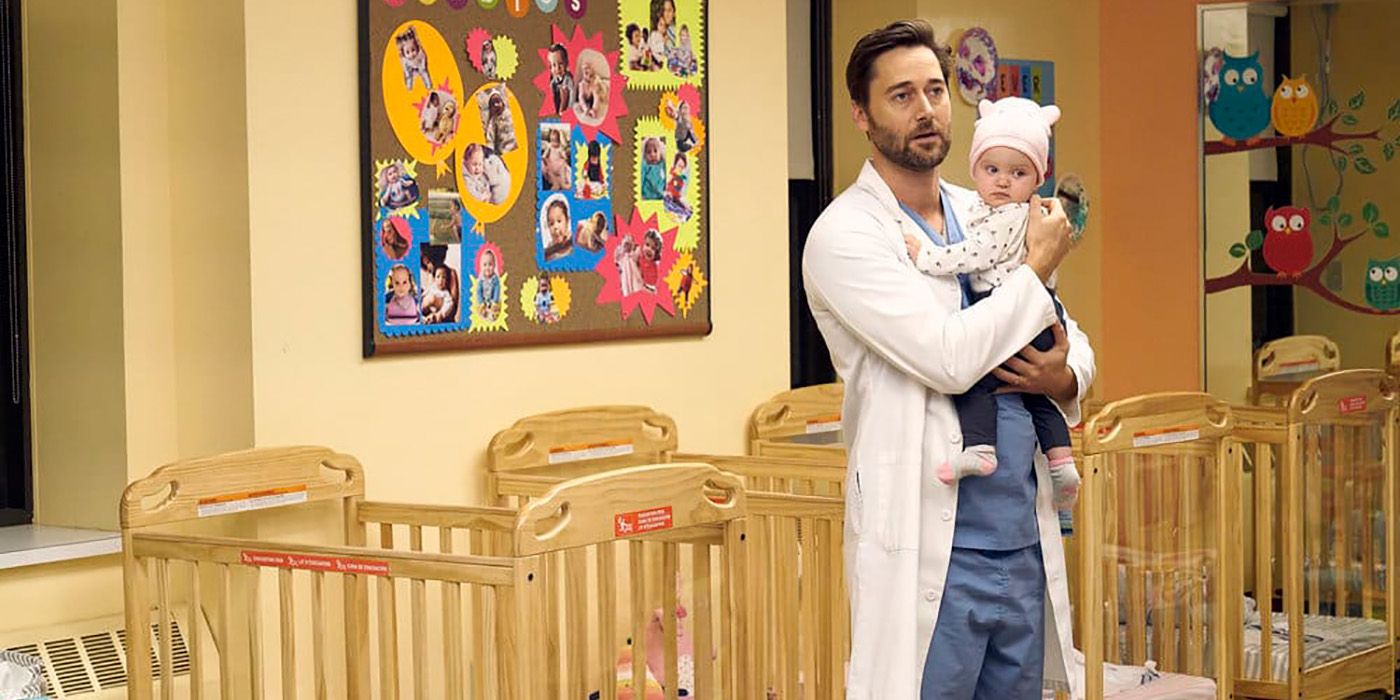 Max standing in the hospital nursery, holding Luna in his hands with several cribs behind him