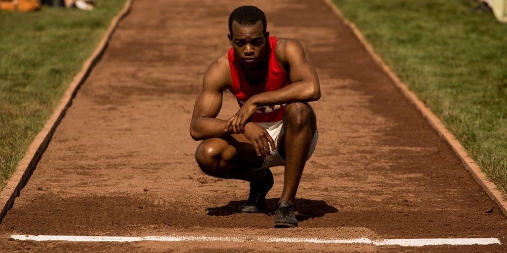 Jesse Owens faz agachamento em uma pista de corrida