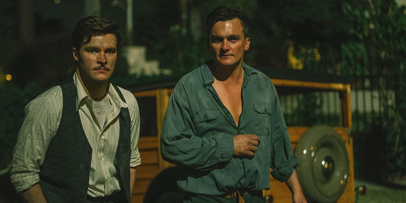 Jack Reynor and Rupert Friend's standing next to each other, at night, in Strange Angel