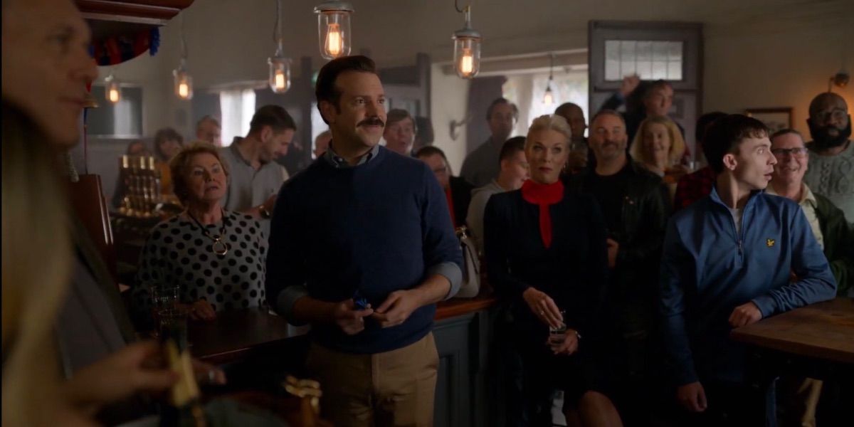 Ted Lasso surrounded by bar patrons