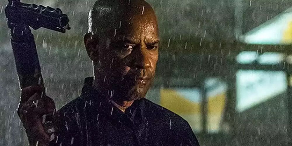 Robert walks with a machine gun in the rain in The Equalizer