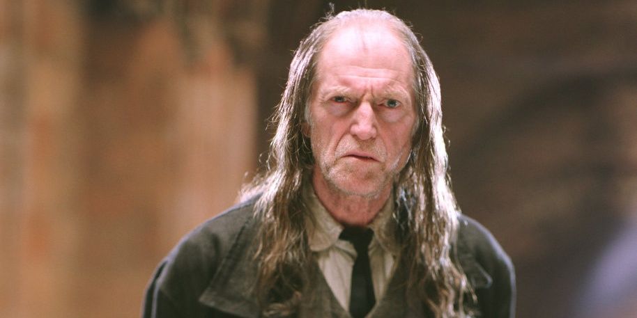 Argus Filch standing inside of Hogwarts.