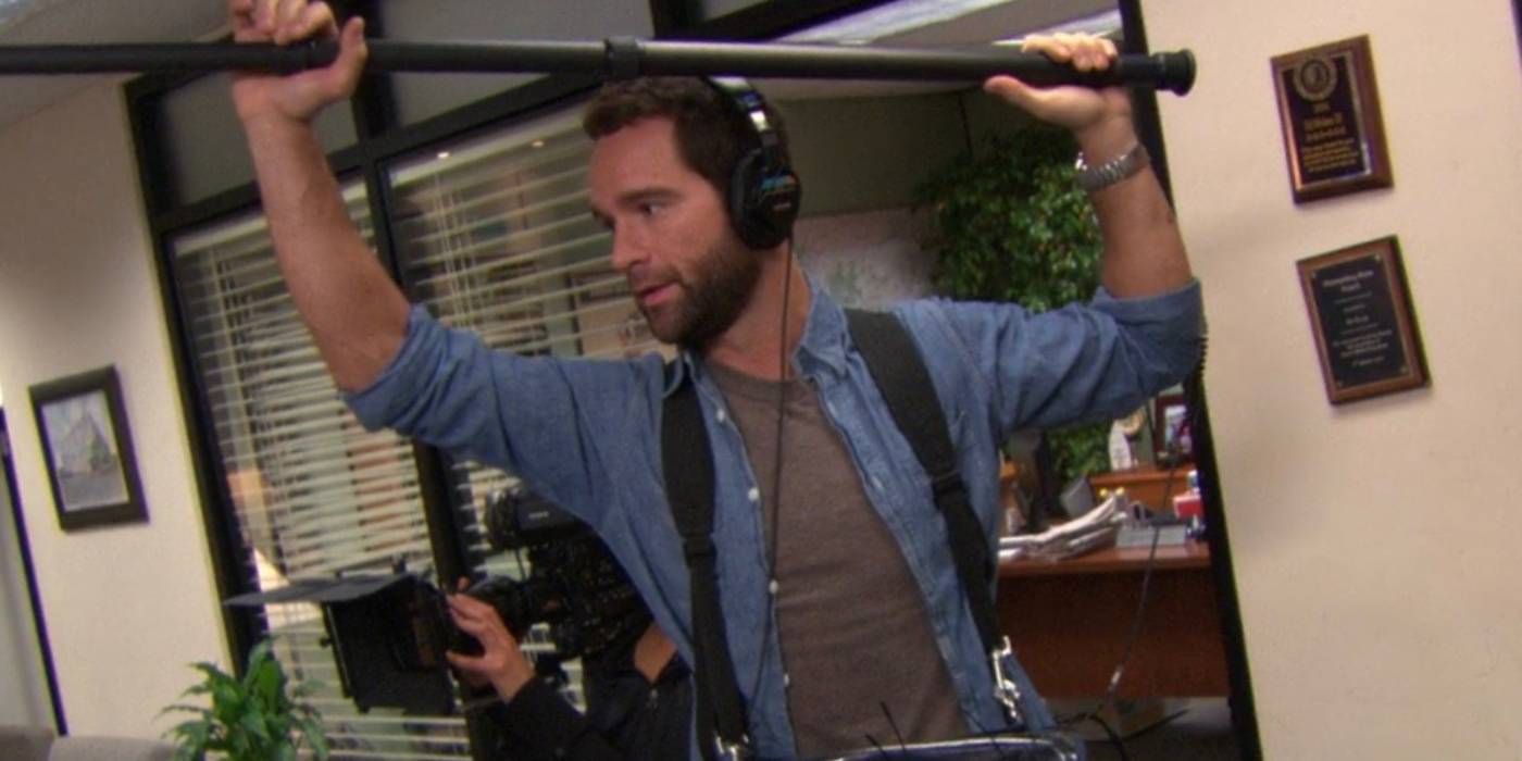 Chris Diamantopoulos como Brian segurando o microfone Boom no escritório