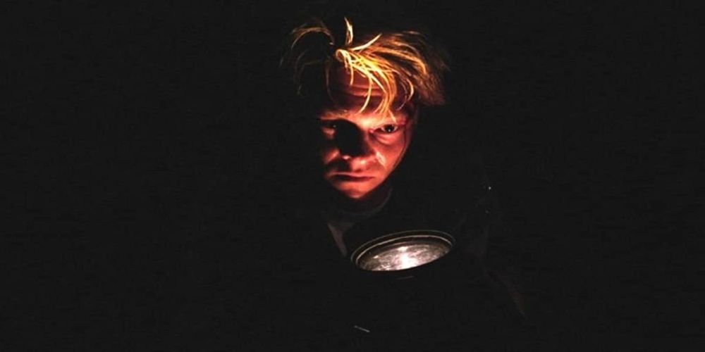 A character in Villmark shrouded in darkness and holding a flashlight to her face