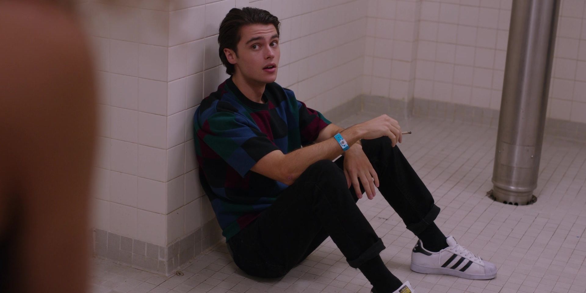 Marcus Baker from Ginny &amp; Georgia sits on the floor of the school bathroom smoking a joint