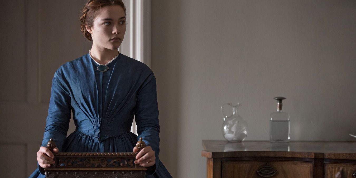 Florence Pugh as Lady Macbeth, in a blue dress and standing in her home