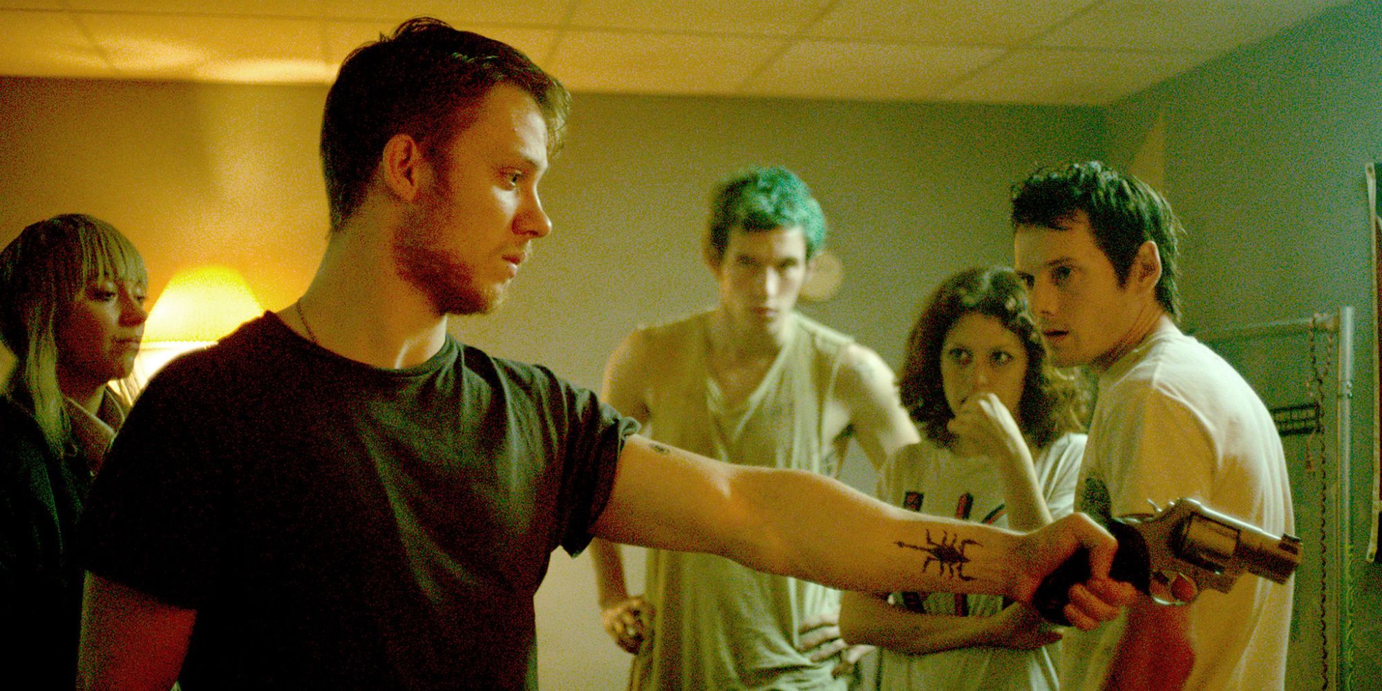 A young man points a gun at someone while three others look on in Green Room