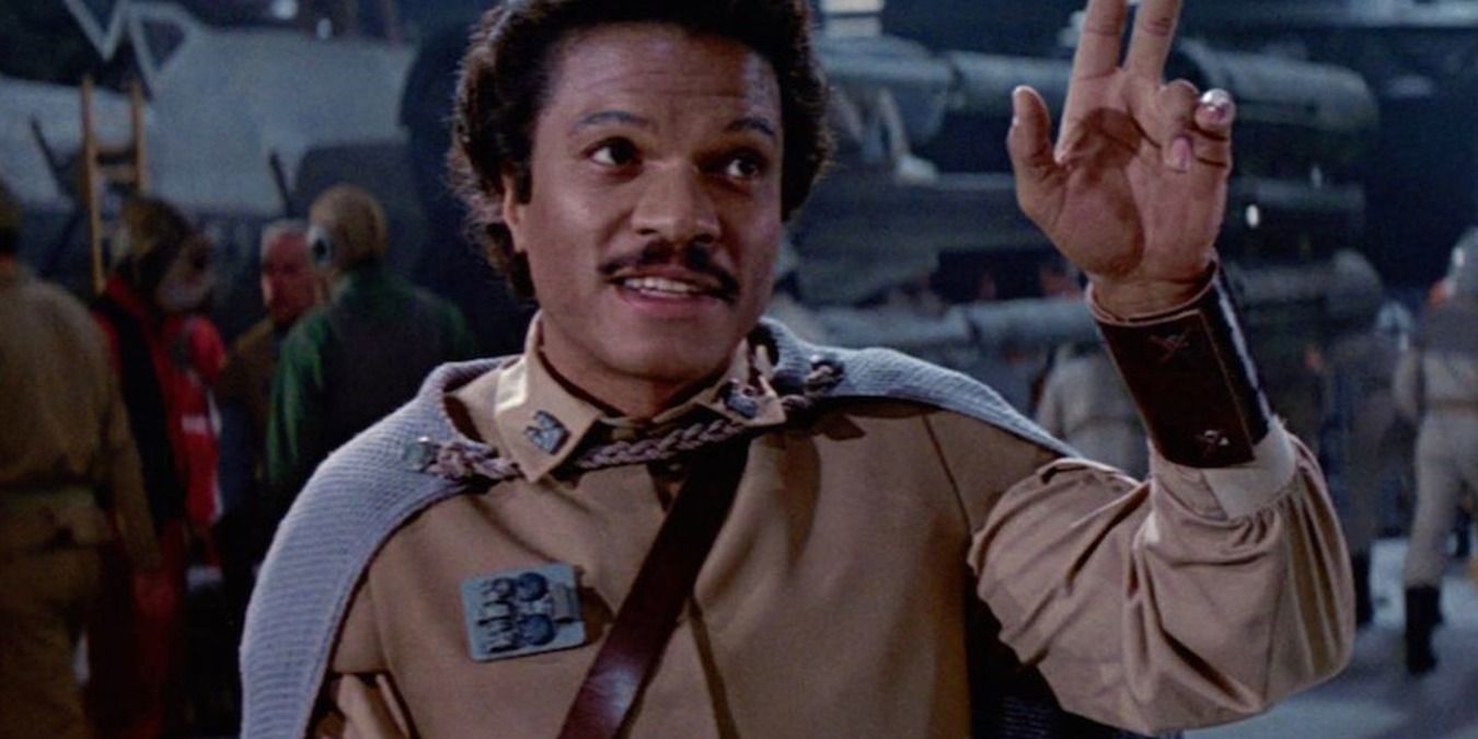 Star Wars's Lando standing in the hanger, smiling and pointing up