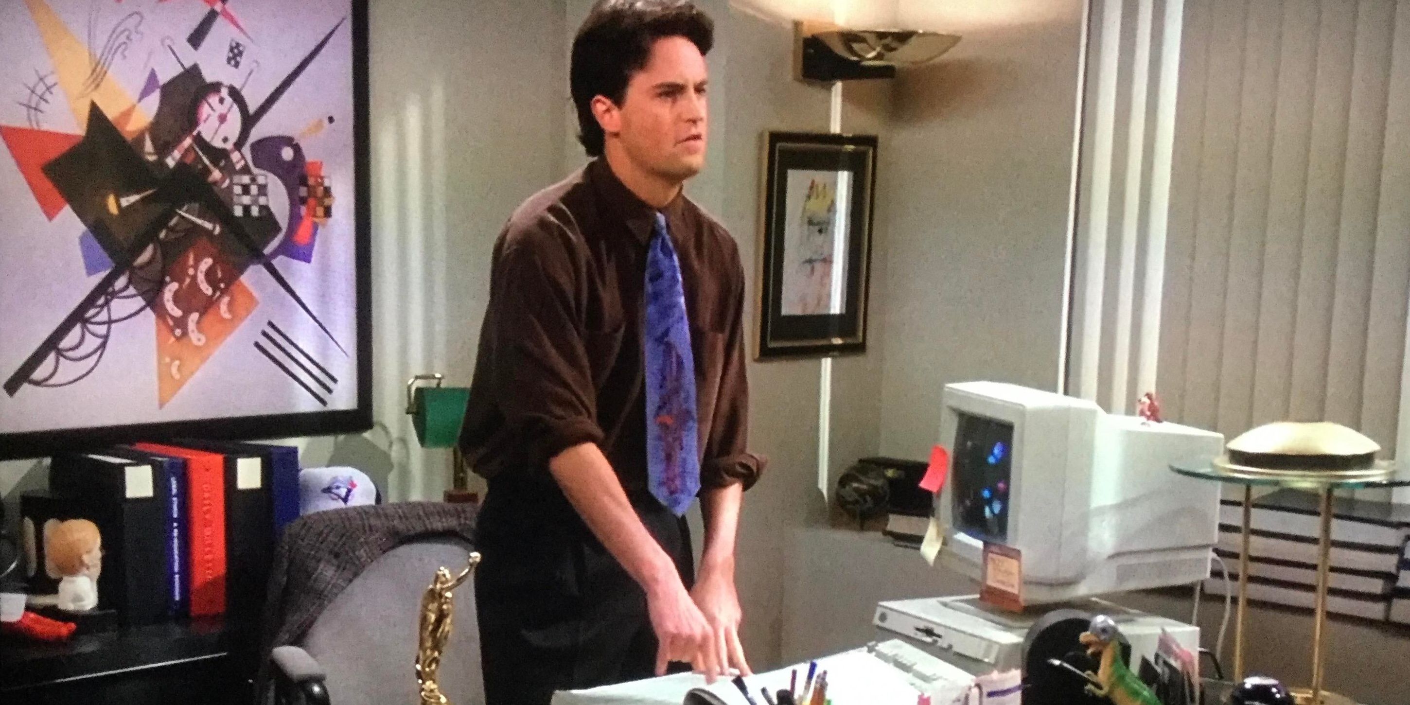 Matthew Perry as Chandler Bing standing next to his desk at work