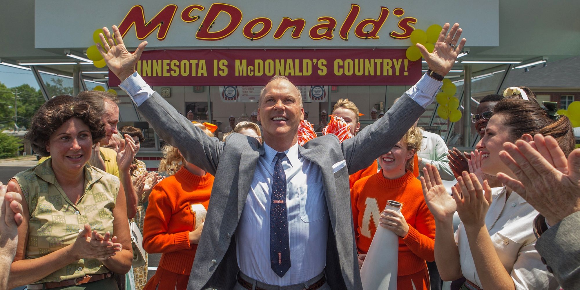 Ray Kroc standing amid a crowd clapping in front of a McDonald’s entrance in The Founder