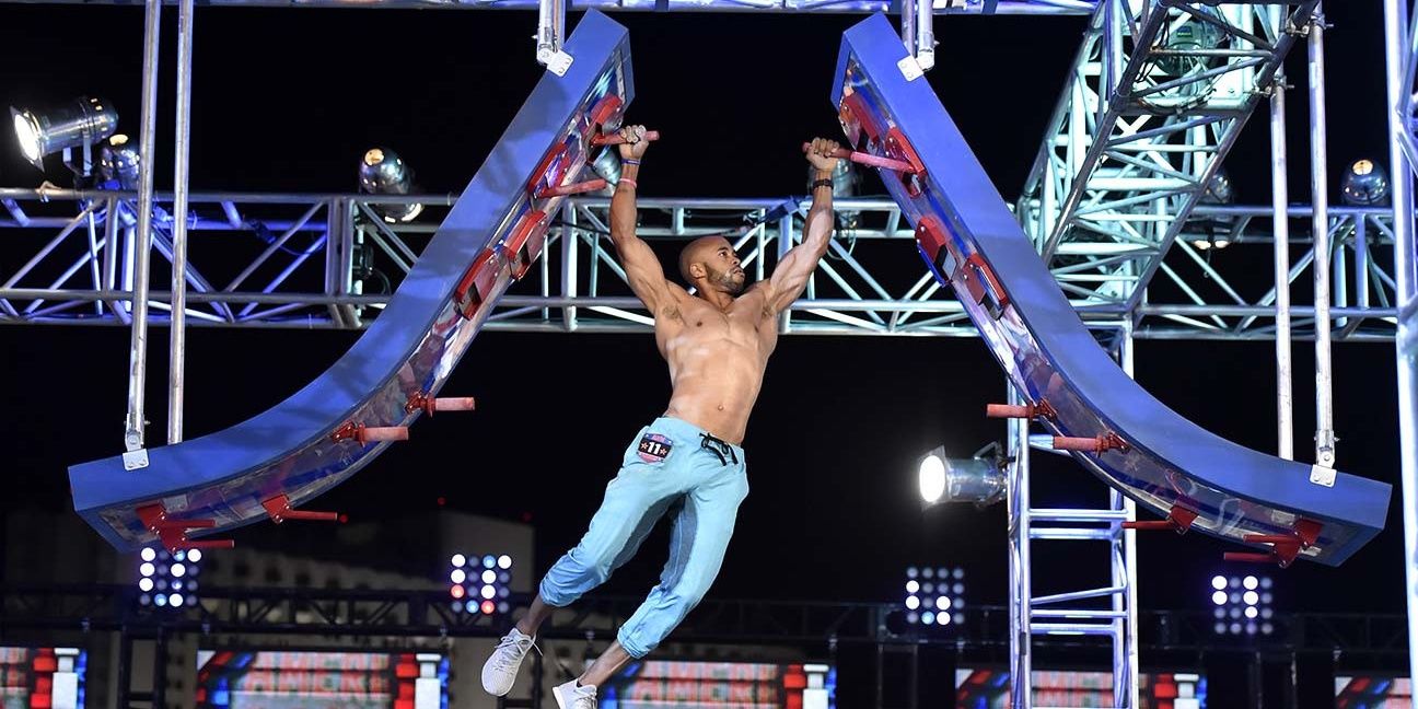 A buff man hangs in the air during American Ninja Warrior