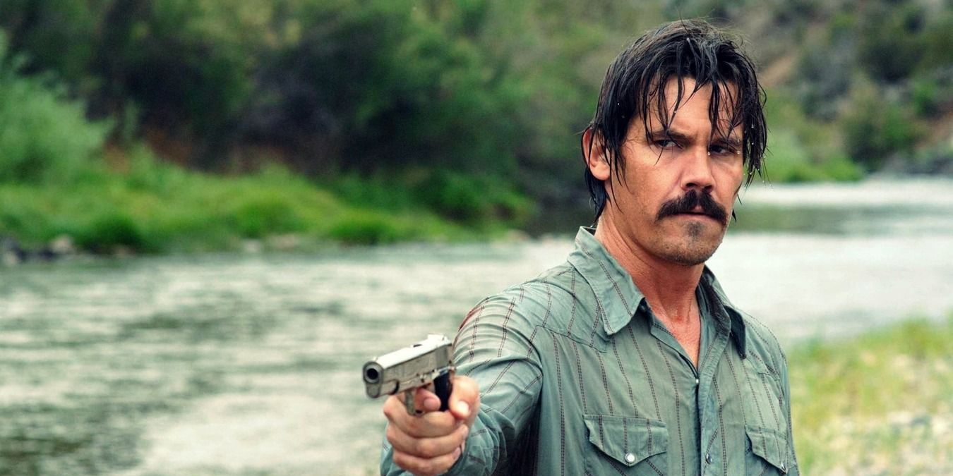 Llewlyn Moss aims his gun by the river in No Country for Old Men.