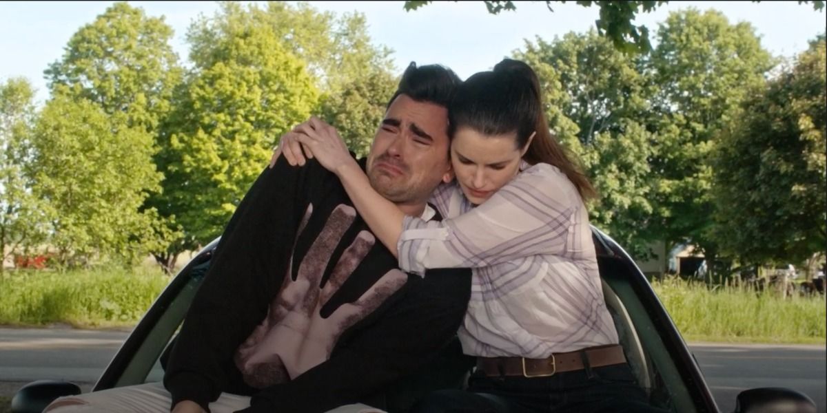 On Schitt's Creek, David and Stevie sitting on a car she is hugging him