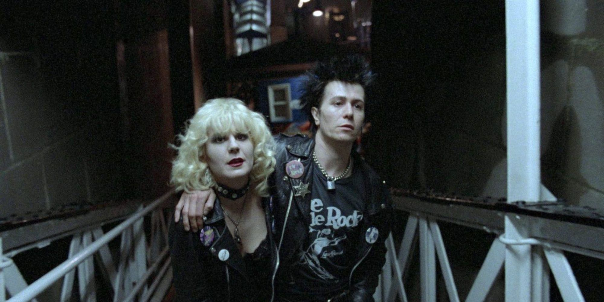 Sid and Nancy walking up a ramp with Sid's arm around Nancy's shoulder in the Sid & Nancy movie.