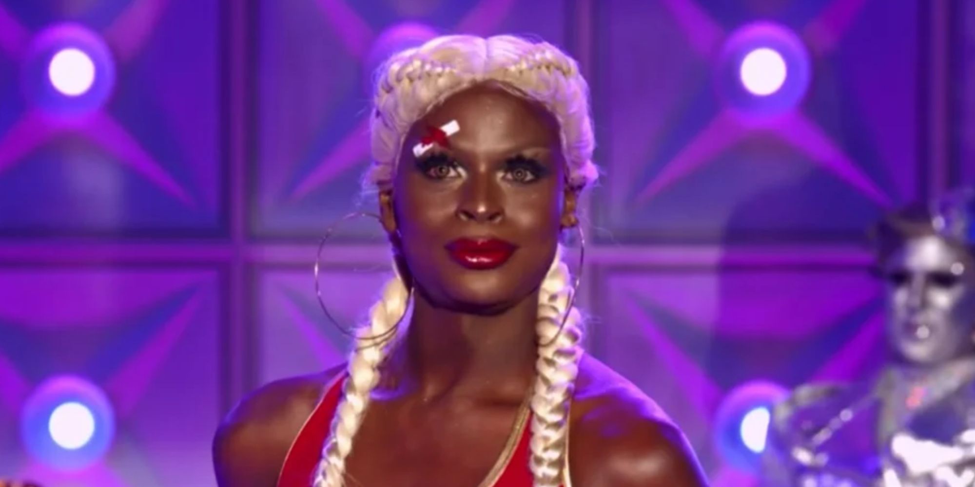 Symone smiling in a white wig on the main stage of RuPaul's Drag Race season 13