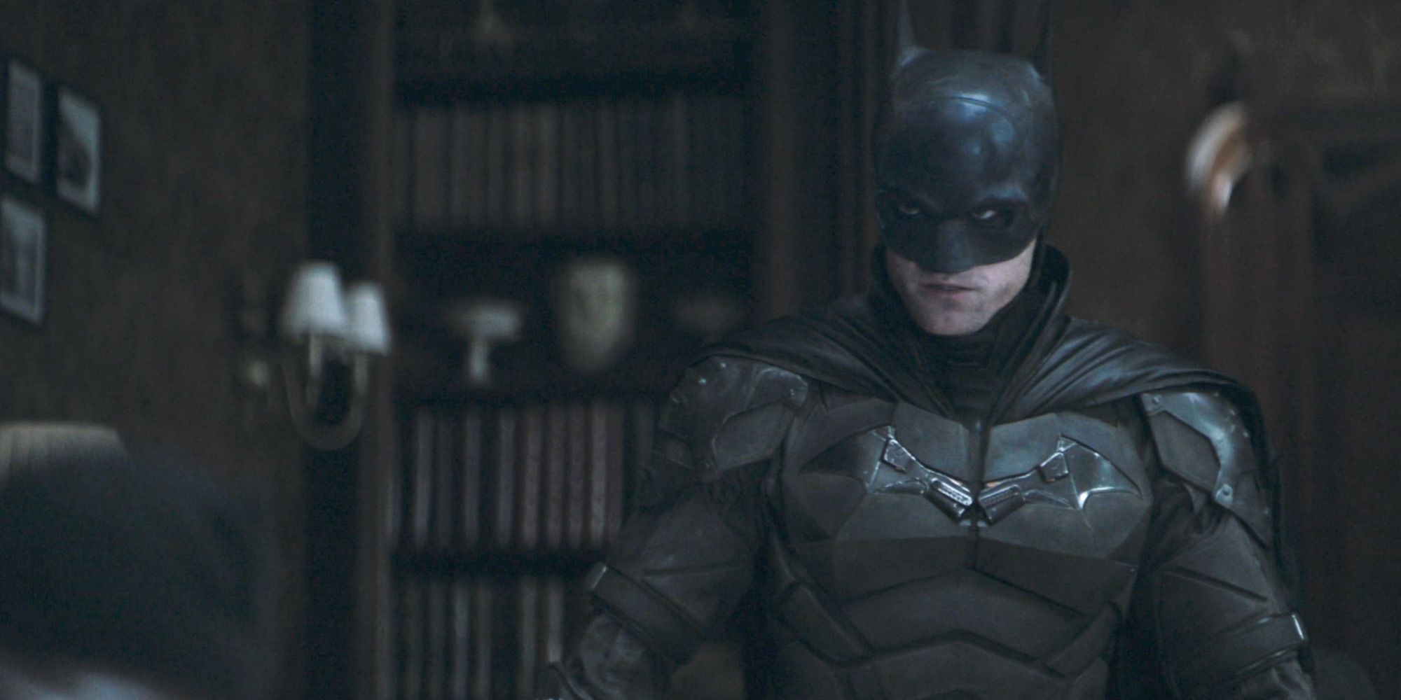 Batman standing in front of bookshelf in dark room