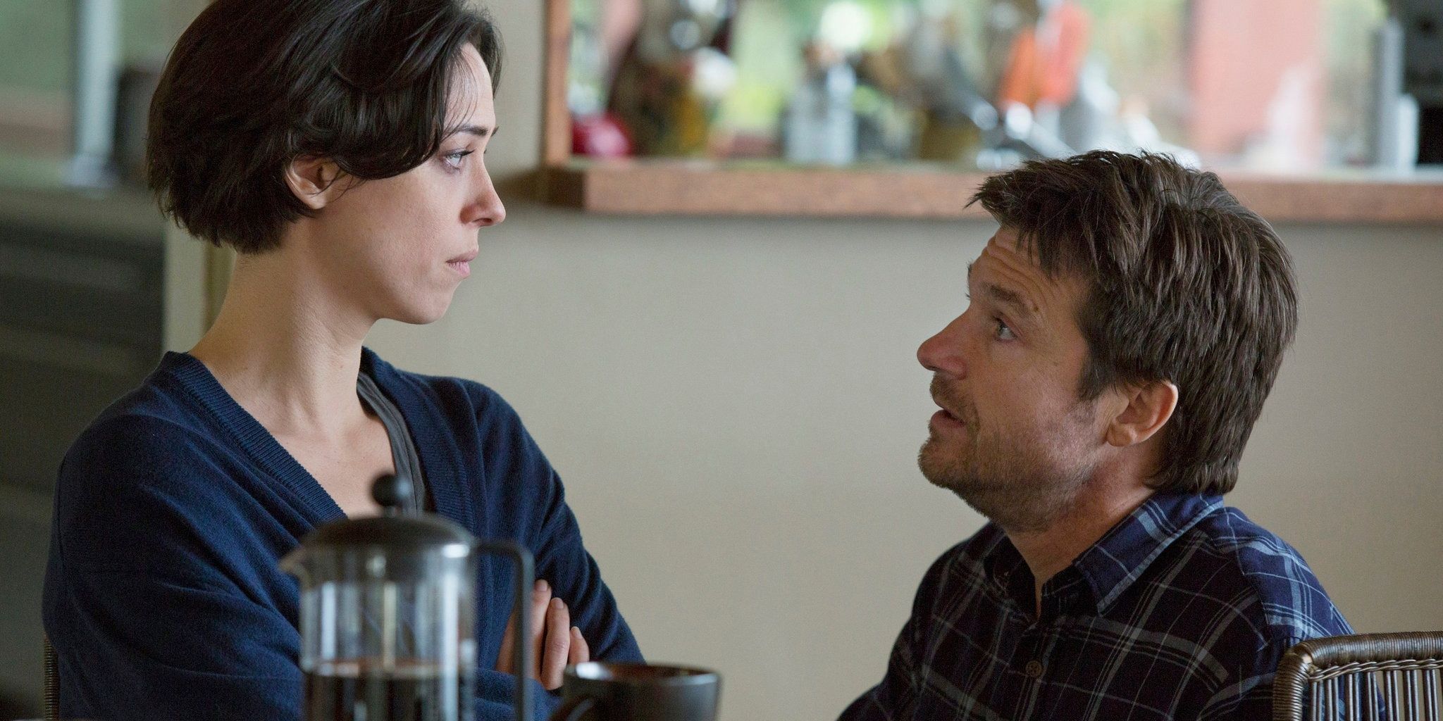 Jason Batemen on his knees talking to Rebecca Hall at the dining table in The Gift
