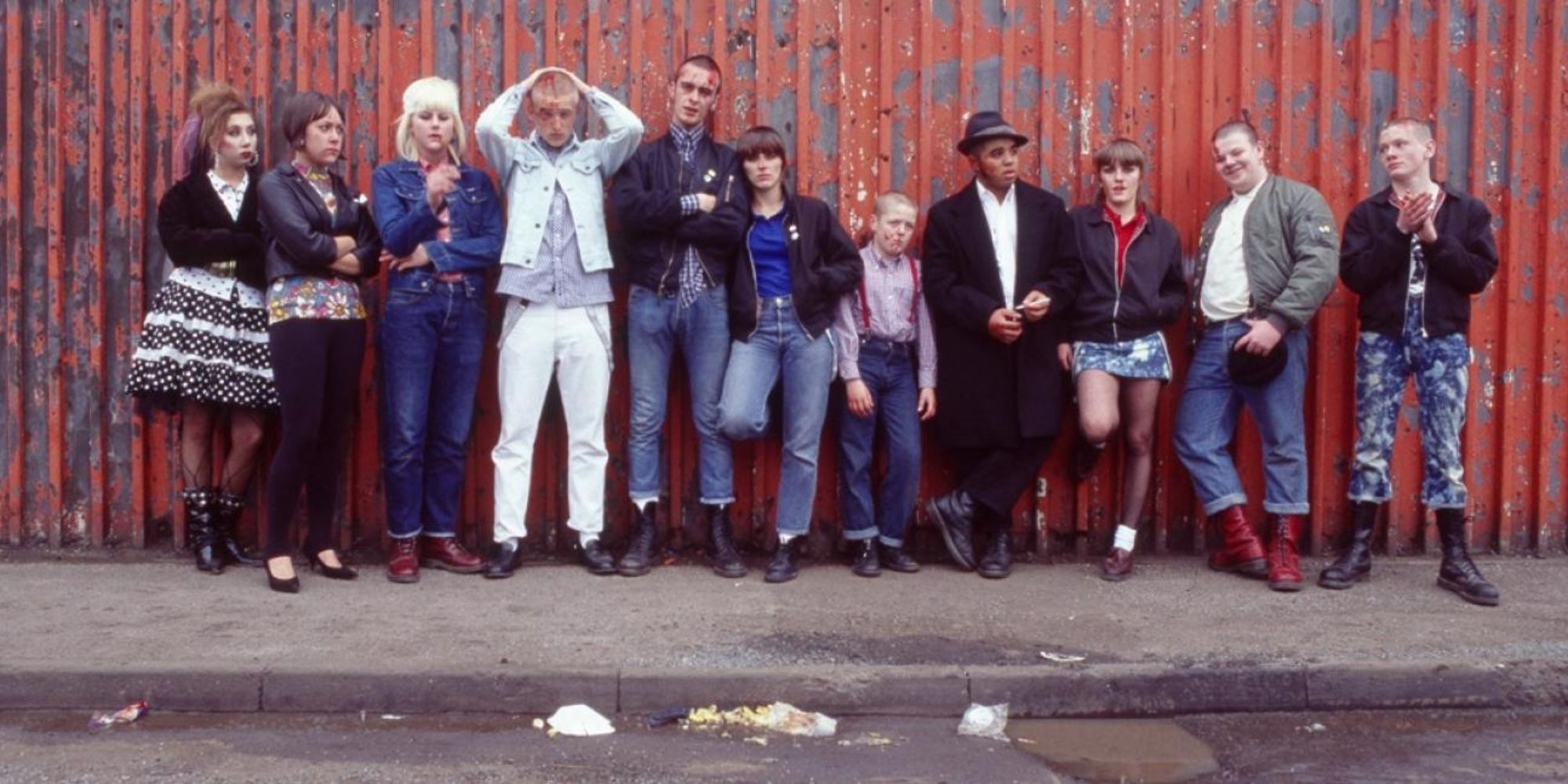Group of punks and misfits leaning up against a corrugated red chipped wall in This is England.