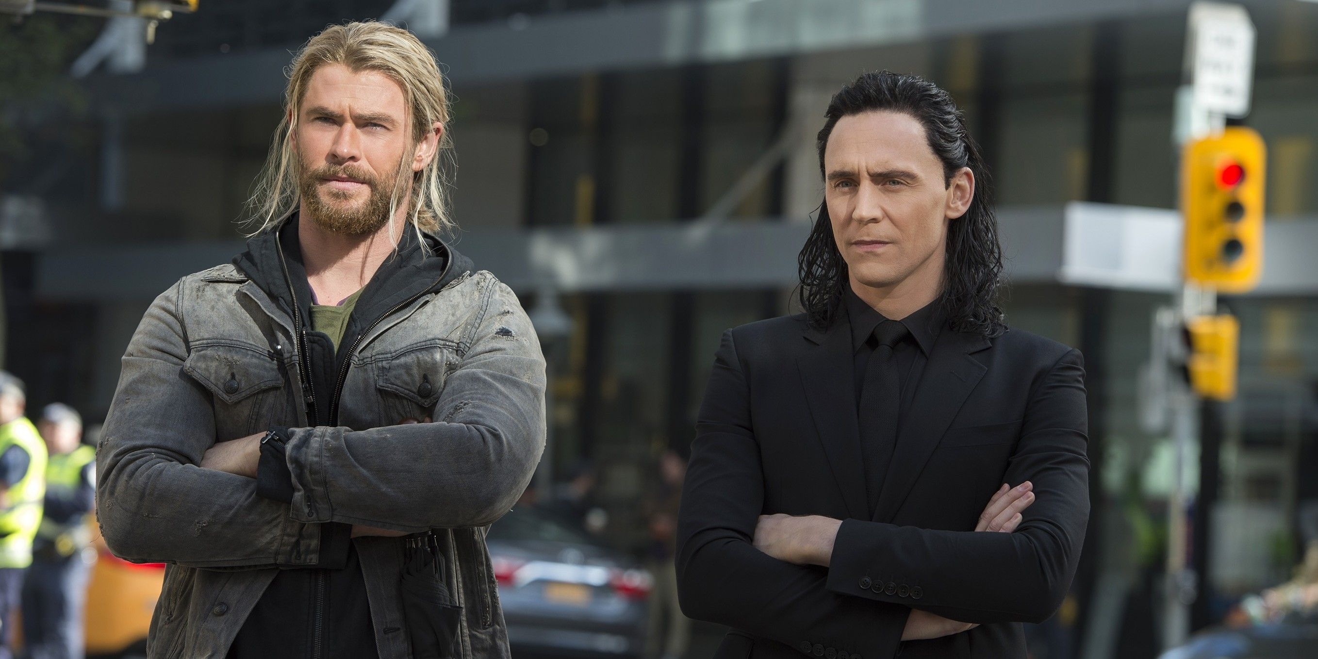 Thor standing with arms crossed beside Loki on city street