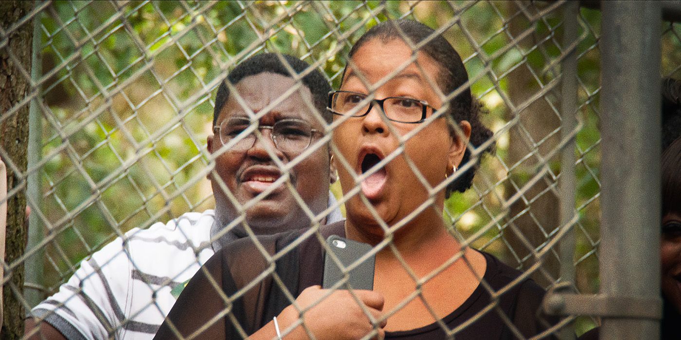 A woman standing behind a fence with her mouth wide open in stock, Lil Rel behind her in Bad Trip