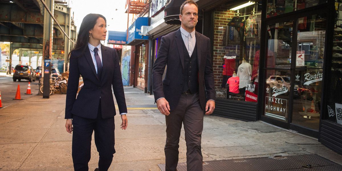 Dr. Joan Watson (Lucy Liu) and Sherlock Holmes (Jonny Lee Miller) strolling through a Manhattan construction site