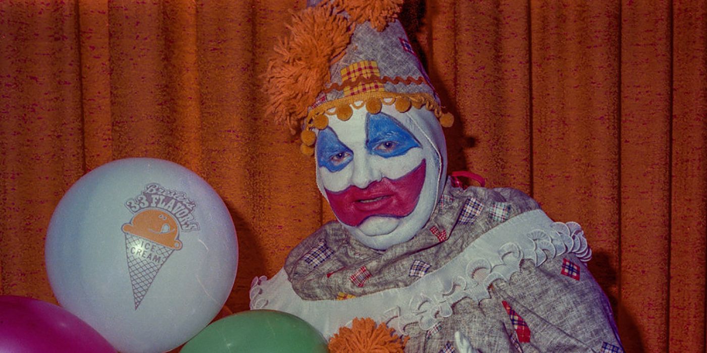 John Wayne Gacy wearing a clown costume and holding balloons.