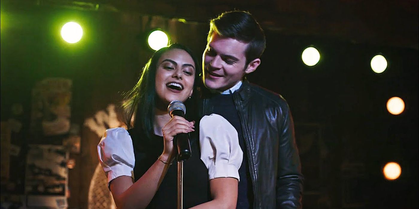 Veronica singing with a microphone in her hand while Chadwick hugs her from behind and looks over her shoulder.