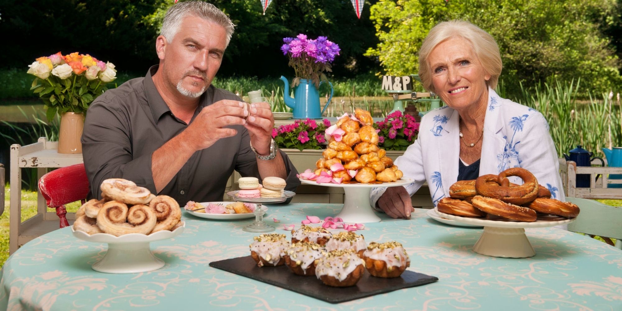 Mary Berry and Paul Hollywood sat at a table with cakes in GBBO