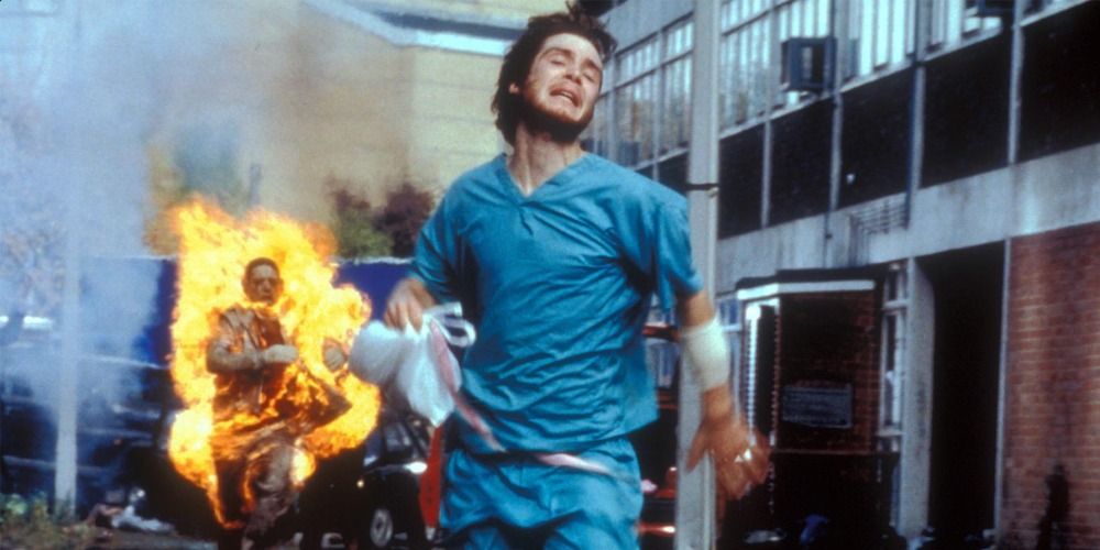 Jim in hospital garbs running from a zombie on fire in a scene from 28 Days Later