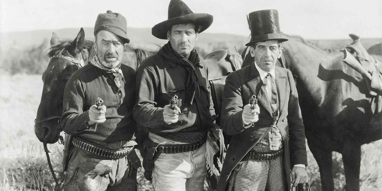 Black and white still from 3 Bad Men with three men pointing guns at camera.