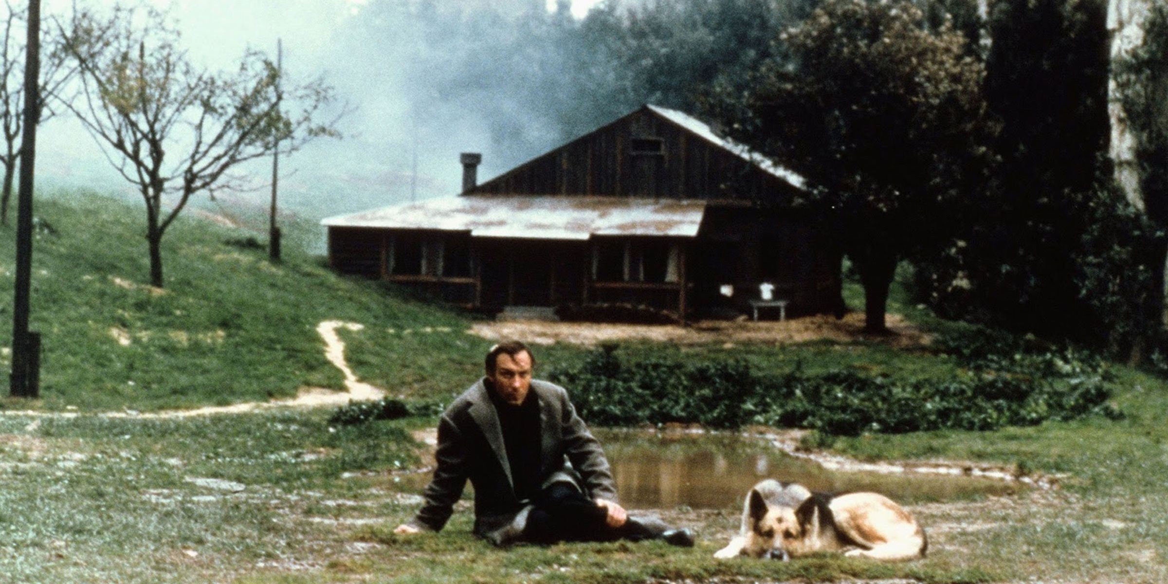 A man sitting on the ground along with a German shepherd in a still from Nostalghia