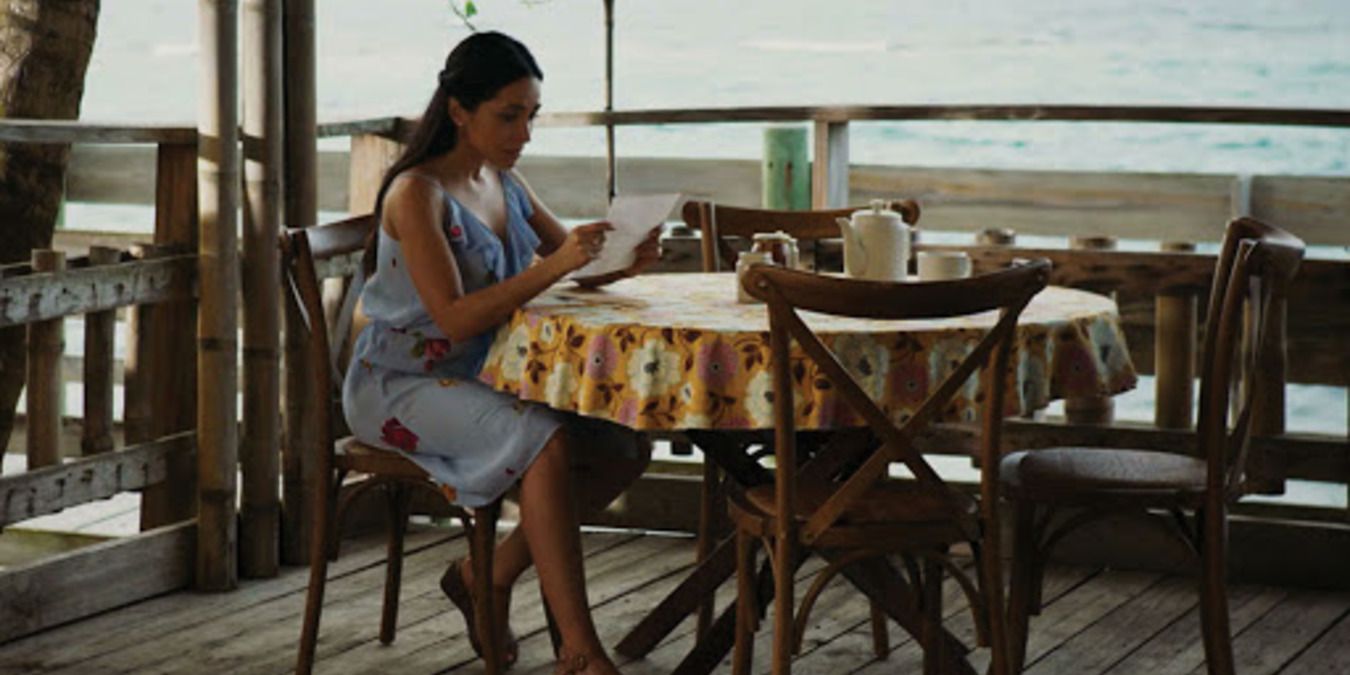 Ana Isabelle as Anita, sitting at a table by a beach in Imprisoned