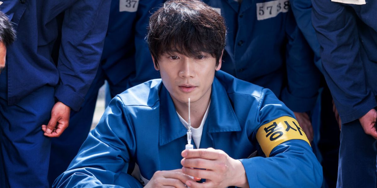 Yo-Han vestindo uniforme de prisão segurando seringa em Doctor John