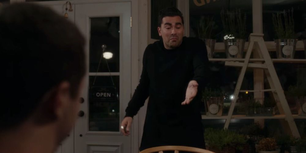 David standing up and talking in front of Patrick in Schitt's Creek