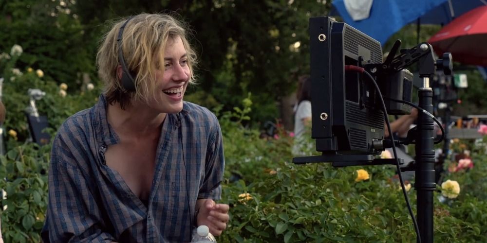 Greta Gerwig wearing headphones and laughing at something on a screen