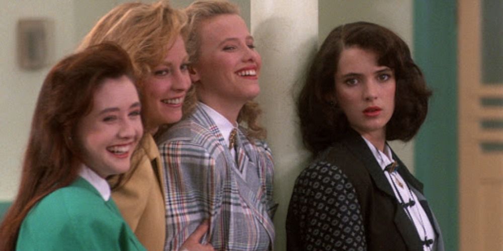Heather, Heather, and Heather laughing at something off-camera while Veronica looks center in a scene from Heathers