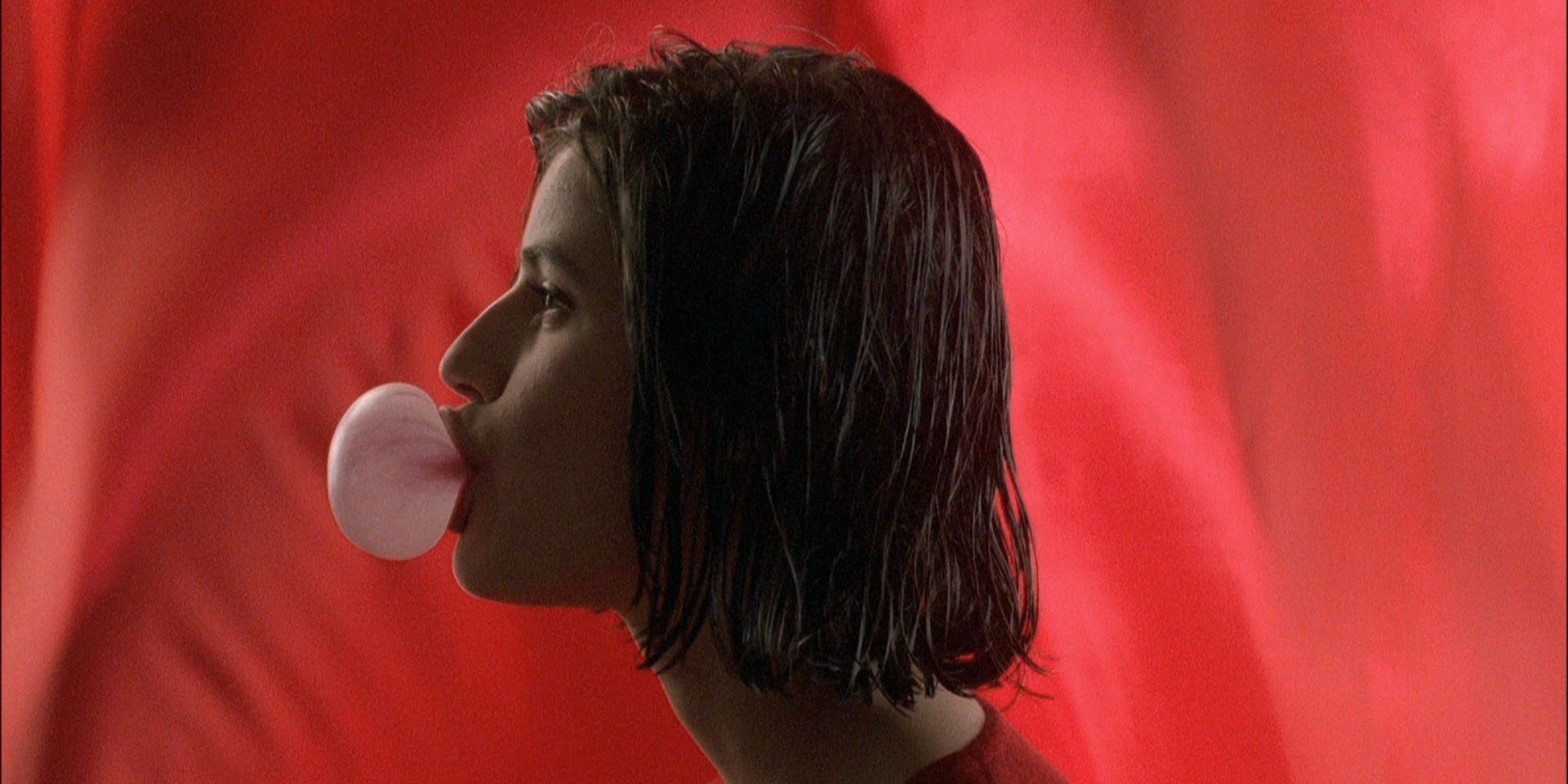 Irène Jacob as Valentine Dussaut blowing a bubble gum with a red background behind her