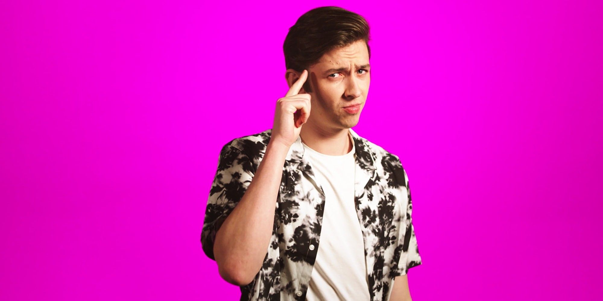 A headshot of Jack from The Circle, finger to his temple, with a purple-pink background.