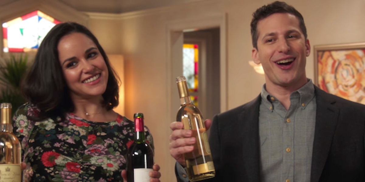 Jake and Amy smile with wine bottles