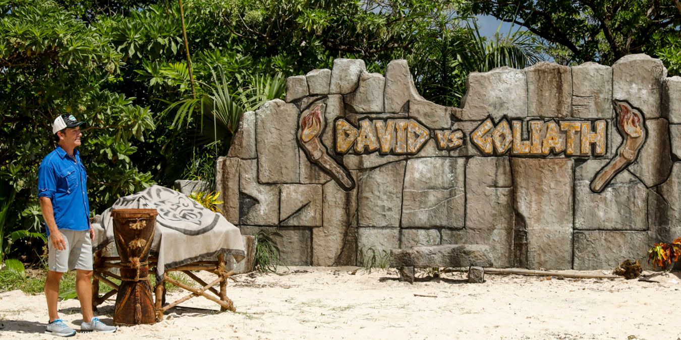 Jeff Probst standing in front of a rock that reads 'David vs Goliath' before a challenge